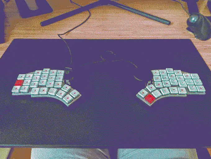 
              A splitkb.io halcyon kyria keyboard. It's split in two halves, has white keycaps with red lettering and features a display as well as a trackpad module 
            