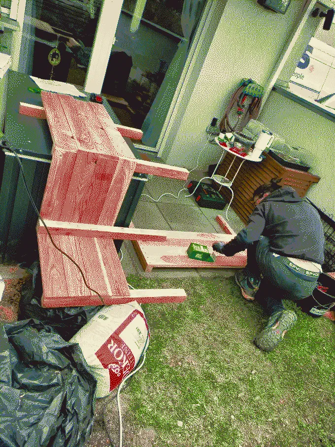 
              Dominik kneeling on the ground screwing together a side wall of the planter. Next to him is the rest of the planter resting on the toolbox
            
