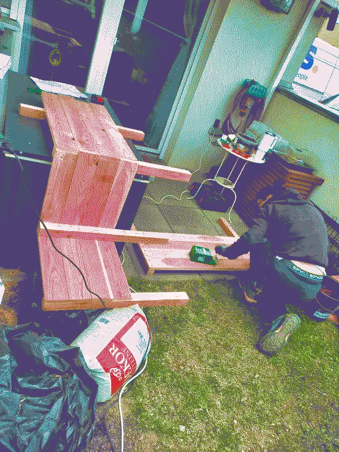 Dominik kneeling on the ground screwing together a side wall of the planter. Next to him is the rest of the planter resting on the toolbox